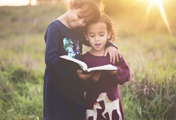 girl's left hand wrap around toddler while reading book during golden hour