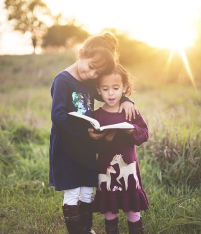 girl's left hand wrap around toddler while reading book during golden hour